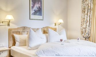 A cozy bedroom with a large bed and white pillows. A picture hangs on the wall, and there are several light sources for a warm atmosphere.