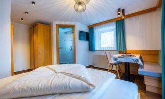 A cozy room with a double bed and wooden cabinets. By the window, there is a table with chairs and a small television.