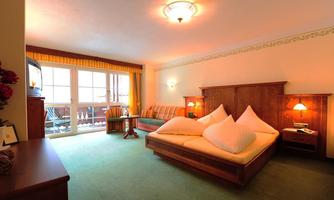 A cozy hotel room with a double bed and a seating area. Large windows let in plenty of light and provide access to a balcony.