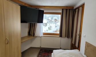 A simple bedroom with a bed, a wardrobe, and a television. Outside the window, you can see snow-covered landscapes.
