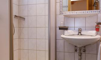 A modern bathroom with a shower cabin and a sink. The walls are tiled and the space feels clean and inviting.