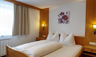A cozy bedroom with a double bed and two large pillows. The walls are made of wood, and there is friendly light as well as a picture featuring floral motifs.