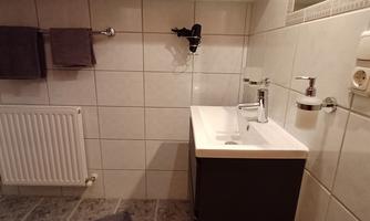 A modern bathroom with a sink and a hanging cabinet. Towels are hanging on the wall and the floor is tiled.