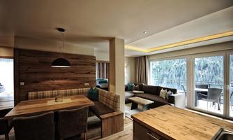 A modern and cozy living room with wooden paneling and a large window that offers a view of nature. The room is stylishly furnished with a seating area and a dining table.
