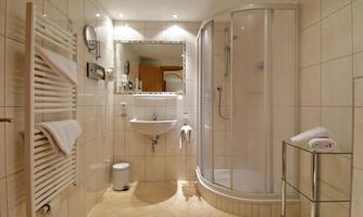 A modern bathroom with a shower, sink, and a towel warmer. The walls are tiled and the lighting is bright.