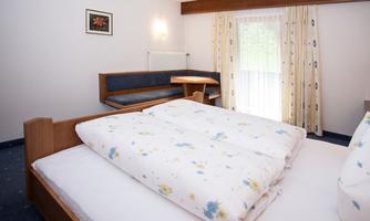 A cozy room with a double bed and a sofa bed. Large windows let in plenty of daylight, and the decor is simple and inviting.