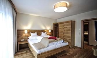 A modern bedroom with wooden details and a comfortable double bed. Large windows provide plenty of daylight and a cozy atmosphere.