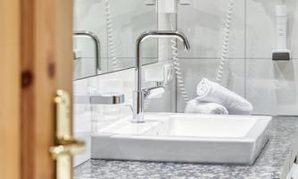 A modern bathroom with a white sink and an elegant faucet. In the background, fresh towels are placed on the countertop.