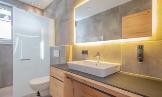 A modern bathroom with an elegant design. There is a large mirror light and a dark countertop.