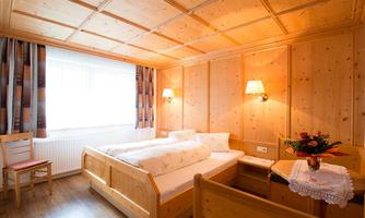 A cozy bedroom with two wooden single beds. Large windows bring a lot of daylight into the room.