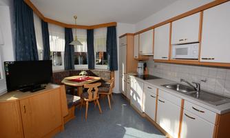 A bright kitchen with a round dining table and chairs. The kitchen furnishings are modern, featuring a stove, refrigerator, and microwave.