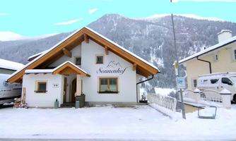 A charming wooden house in the snow with the inscription "Sonnenhof". Snow-covered mountains can be seen in the background.