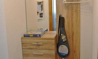 A modern hallway with a wooden wardrobe and a large mirror. A coat hanger and a bag are hanging on the wall.