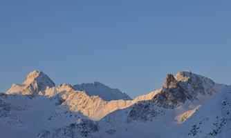 An impressive mountain landscape with snow-capped peaks. The sky is clear and blue.