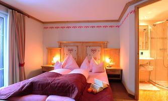 A cozy bedroom with a double bed and two lamps. In the background, a modern bathroom can be seen.