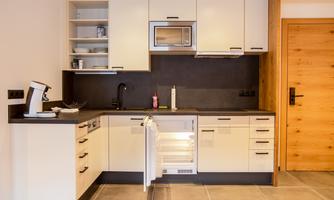 A modern kitchen with light cabinets and a dark workspace. The refrigerator is open and turned to the side.