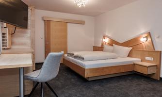 A modern hotel room with a large bed and a desk. The decor is bright and minimalist.