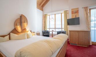 A cozy bedroom with a large bed and warm wooden elements. The large windows provide plenty of daylight and a pleasant atmosphere.