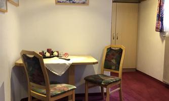 A cozy room with a table and two chairs. The walls are light, and the floor is covered with red carpeting.