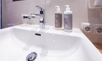 A modern sink with a shiny faucet. Next to the sink are two bottles of care products.