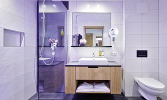 A modern bathroom with a glass shower and a stylish wooden sink. Bright tiles and a large mirror area create an inviting atmosphere.