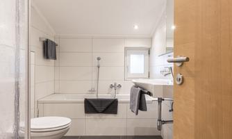 A modern bathroom with a bathtub and a sink. The walls are tiled in bright colors and there is a wooden half decoration.
