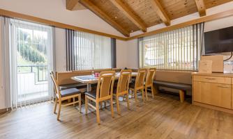 A cozy dining area with wooden chairs and a large table. The windows provide plenty of daylight and a view of the outdoors.