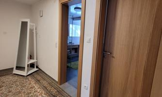 A bright hallway with a carpet and two doors. On the left side, there is a coat rack.