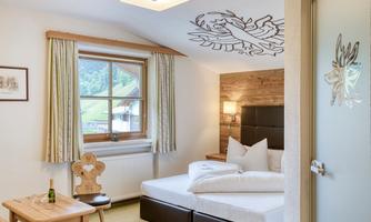 A cozy room with a double bed, a small table, and a window overlooking the landscape. The walls are lovingly decorated, and the overall ambiance conveys an inviting atmosphere.