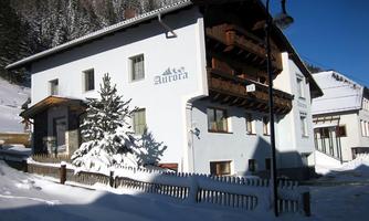 A house in winter snow with a wooden balcony. In the background, snow-covered mountains can be seen.