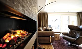 A modern living room with a cozy fireplace and a comfortable armchair. Large windows provide plenty of light and a view outside.