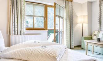 A bright room with a large window and a balcony. The decor is modern and cozy with a comfortable bed and a seating area.