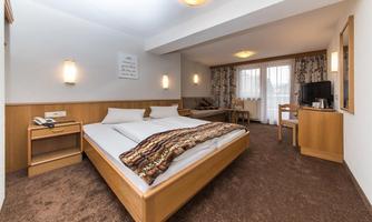 A cozy hotel room with a double bed and modern decor. There is a desk, a television, and large windows with curtains.
