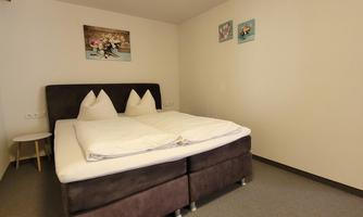 A simple room with a large double bed.  
Some pictures are hanging on the wall, and the floor is carpeted.
