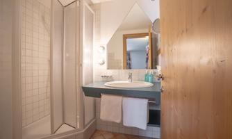 A small bathroom with a shower and a sink. The walls are tiled, and there is a large mirror.