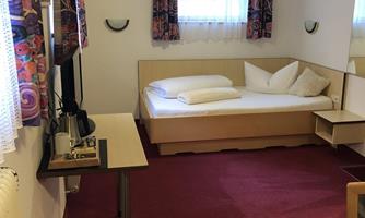 A simple room with a bed and a table. There is a window and colorful curtains that let in light.