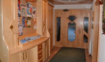A bright hallway with wooden shelves and informational materials. The entrance door has a decorative glass design.