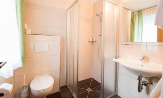 A modern bathroom with a shower, sink, and toilet. Bright tiles and curtains create a friendly atmosphere.