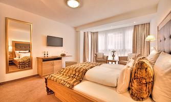 A cozy hotel room with a large bed and modern furniture. There is a window with curtains and a television on the wall.