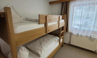 A cozy bedroom with a wooden bunk bed. The room has a neutral carpet and a window with a white curtain.