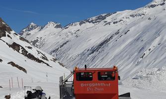 A snowmobile is parked on a snowy mountain road with impressive mountain scenery. The sky is clear and blue, the perfect weather for winter activities.