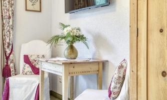 A cozy living area with a small table and two chairs. On the table stands a vase of flowers, and in the background, there is a television on the wall.