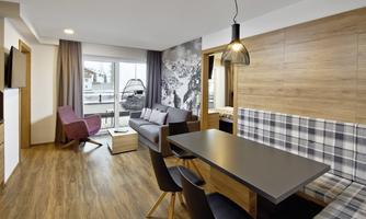 A modern living room with a dining area and a large window. The decor is in warm wood tones and provides a cozy atmosphere.