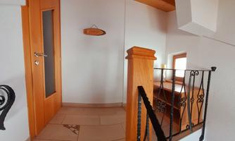 A bright hallway with wood details and a wrought iron railing. The walls are white and the windows let in a lot of light.