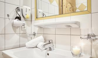 A modern bathroom with a sink, a mirror, and towels. The walls are tiled, and there is pleasant lighting.