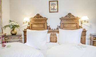 A cozy bedroom with a double bed and large, white pillows. The decor is made of wood and elegantly decorated with stylish lamps and a flower arrangement.
