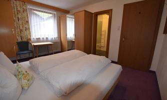A cozy hotel room with two beds and bright windows. There is a table and chairs as well as access to the bathroom.