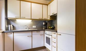 A modern kitchen with white cabinets and wooden details. It is well equipped with a stove, a sink, and a kettle.
