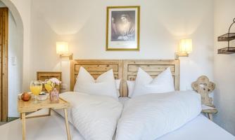 A cozy bedroom with two beds and decorative heart-shaped pillows. Fresh fruits and drinks are on the table.