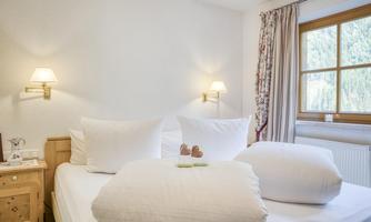 A cozy bedroom with a large bed and soft pillows. In the background, there is a window with a view of nature.